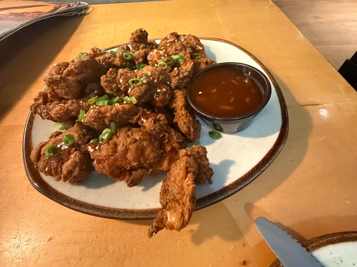 A plate of breaded chicken pieces topped with green onions, with a cup of sweet chili sauce